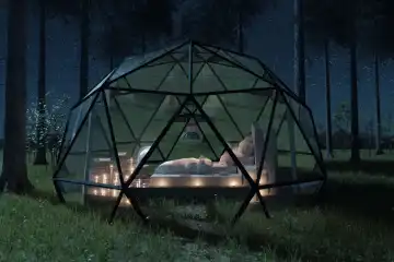 Geodesic domed hut with glass panels in front of a forest landscape at night