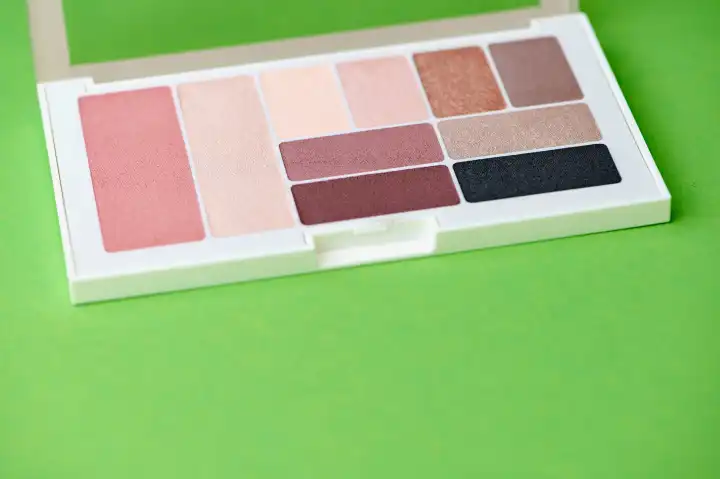 palette with eye shadow and blush of different colors on green background with copy space