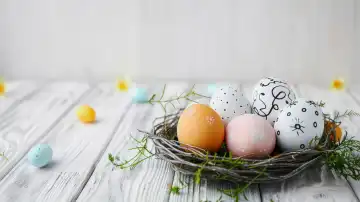 ai generative Illustration eines Osternestes mit bunten Eiern vor weißem Holzhintergrund, Platz für beliebigen Text