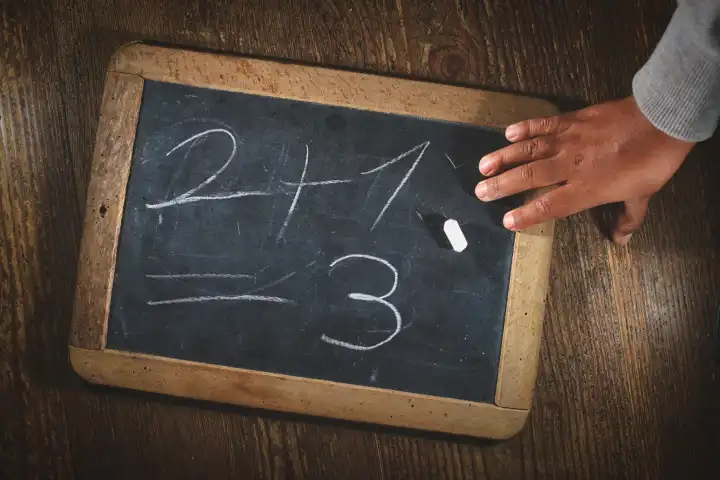 Kinderhand nach dem Schreiben einer einfachen mathematischen Berechnung auf einer kleinen Tafel mit Kreide