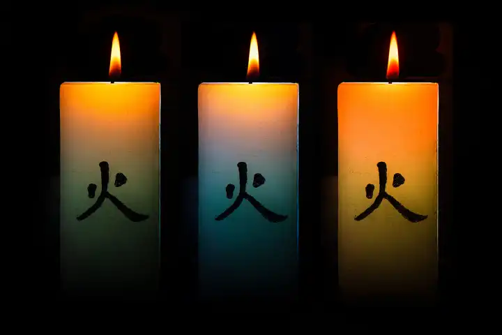 Three Japanese colored burning candles on a black background
