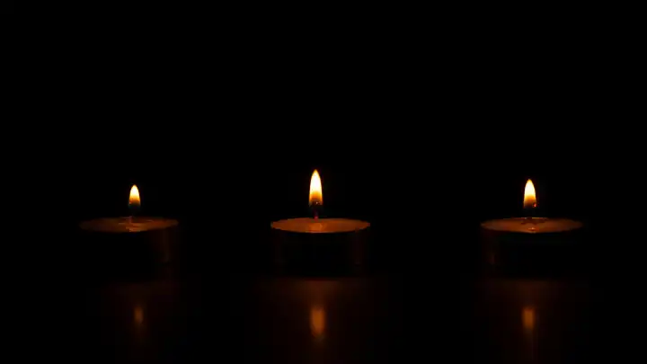 Three lighted wax candles on a black background.