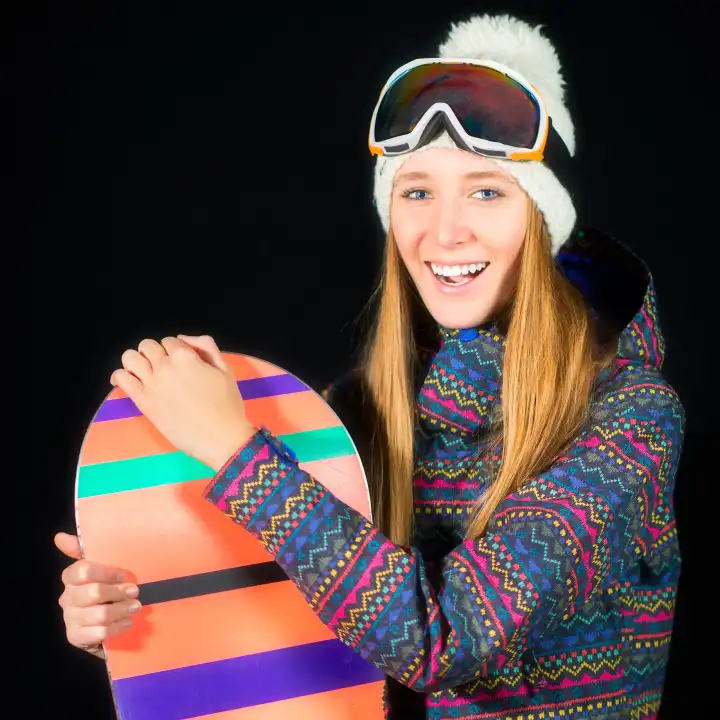 Smiling young girl in ski clothes with snowboard on black background in studio.