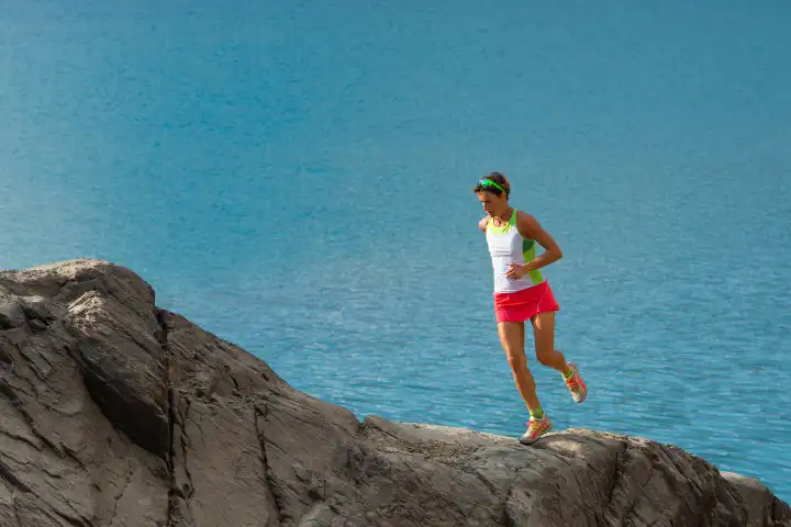 Woman trains running on large rocks on the lake