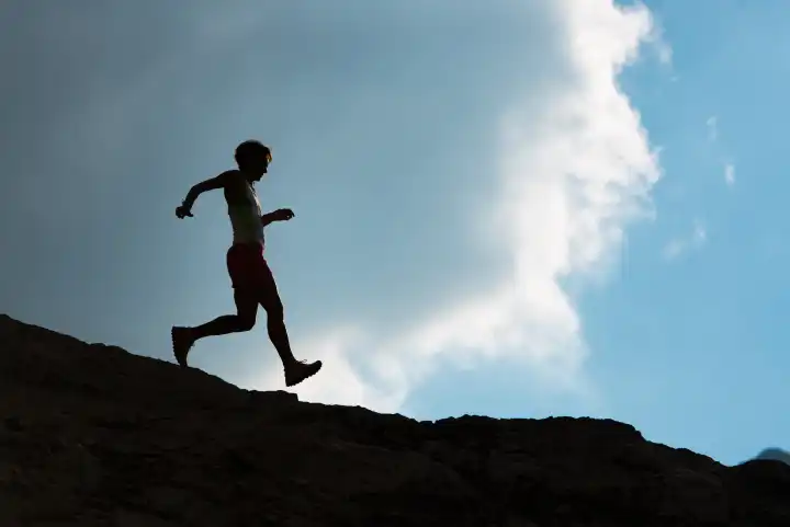 Silhouette of woman running on rocks downhill in the mountains