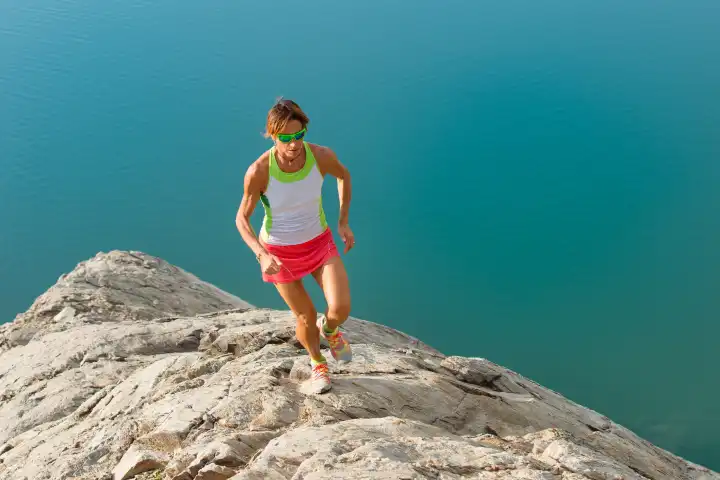 Skyrunner girl runs on a stony back over a lake with concentration