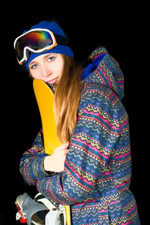Young girl embraces her snowboard in studio on black background.