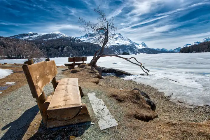 Holzbank zum Bewundern der Landschaft auf dem Eis eines alpinen Sees bei Sankt Moritz in der Schweiz