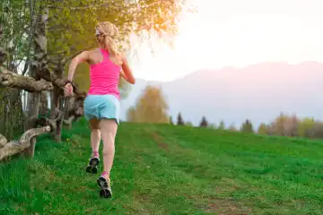Blondes Mädchen Sportler läuft einen Bergpfad in das grüne Gras