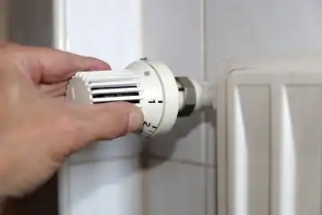 Symbolbild für steigendende Heizkosten: Hand am Thermostat an einem Heizkörper und Geldscheine
