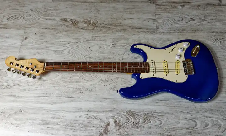 Musik, Pop, Rock: Blaue E-Gitarre, Stratocaster Form, vor weißem Hintergrund mit Holzstruktur