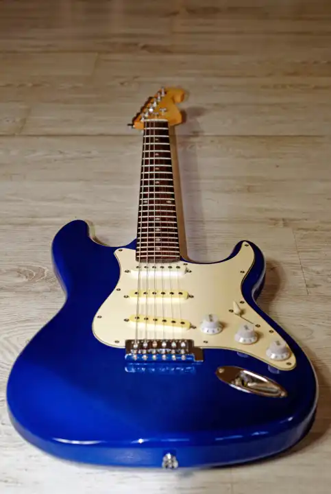Musik, Pop, Rock: Blaue E-Gitarre, Stratocaster Form, vor weißem Hintergrund mit Holzstruktur