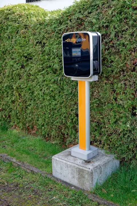 Free-standing charging station for charging electric cars in a parking lot in front of a hedge