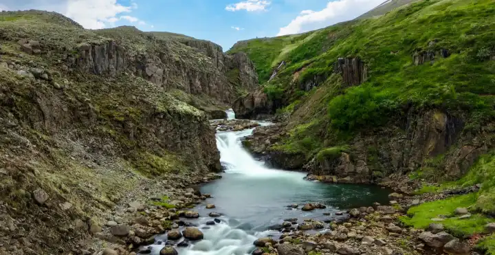 Langzeitbelichtung eines Wasserfalls in einer felsigen Landschaft in Island im Herbst
