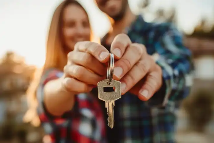 Ein glückliches Paar mit Schlüsseln vor einem schönen neuen Haus, generiert mit KI