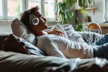 A man sits on a couch and relaxes with headphones while listening to music, generated with AI