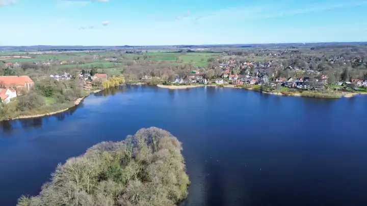 Drohnenansicht eines kleinen Sees bei tiefstehender Sonne, umgeben von Feldern und Wäldern
