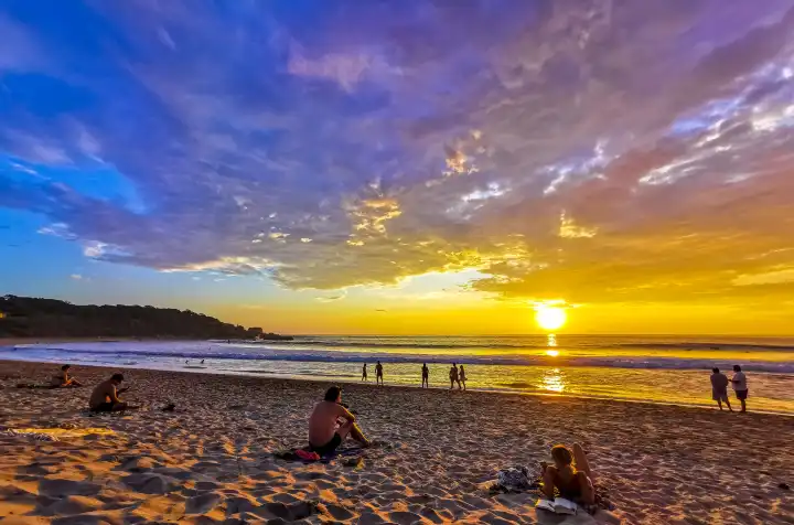 People are watching beautiful stunning colorful and golden sunset in yellow orange red on beach and big wave panorama in tropical nature in Zicatela Puerto Escondido Oaxaca Mexico.