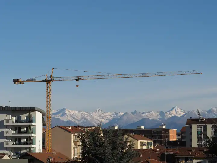 tower crane in a construction site in front of urban skyline with mountains in the background