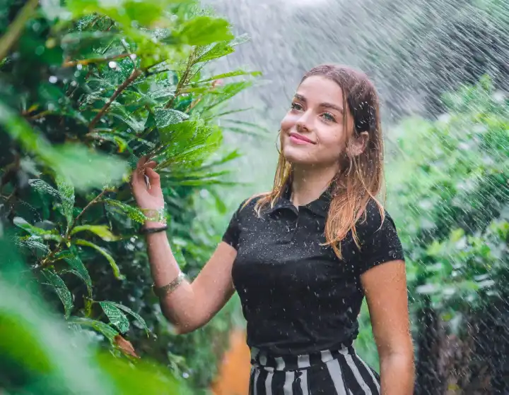 schöne elegante Frau in üppiger Vegetation draußen im Regen in schwarzem Kleid, AI generiertes Bild