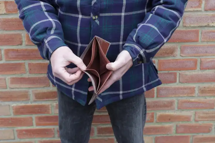 Mann ohne Geld zeigt leeres Portemonnaie mit Backsteinwand dahinter