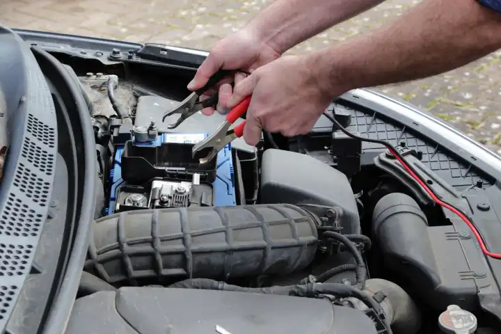 Hände mit Kabeln, die eine Autobatterie im Motorraum aufladen