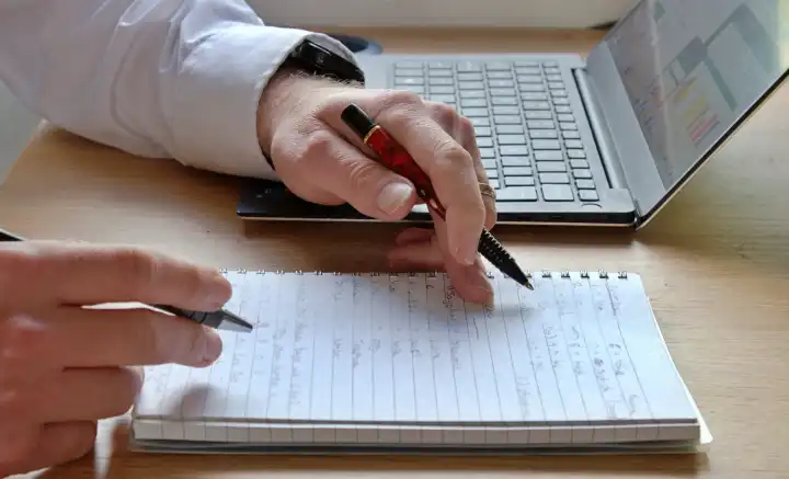 Geschäftsbesprechung mit Laptop und zwei Händen über einem Notizblock im Büro
