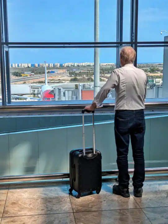 Mann am Flughafen schaut aus dem Fenster auf Flugzeuge