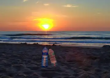 Zwei Plastikflaschen an einem Strand bei Sonnenuntergang